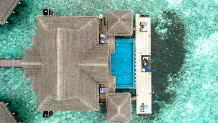 Stunning aerial view of a luxury villa with a swimming pool in the Maldives over turquoise waters.